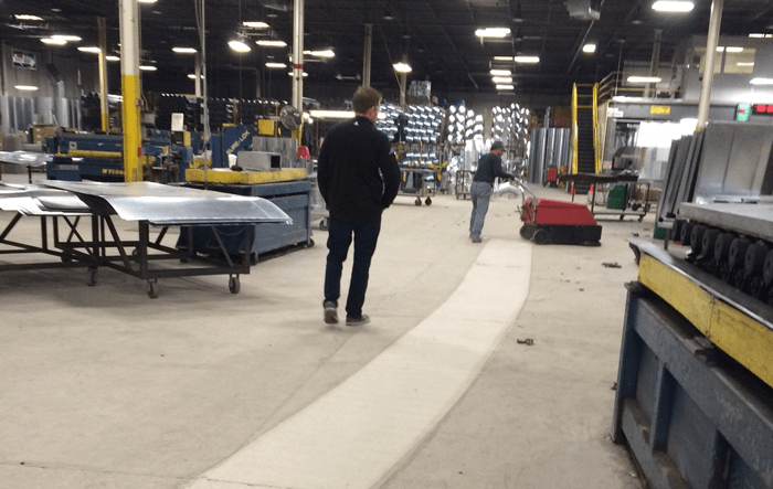 worker pushing factory cat industrial floor sweeper across dusty machine shop floor